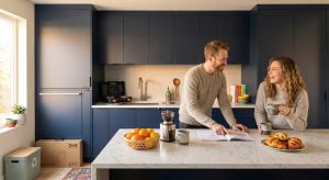 A happy couple reviewing assembly instructions in a modern navy blue IKEA flat pack kitchen with a marble island and integrated appliances.