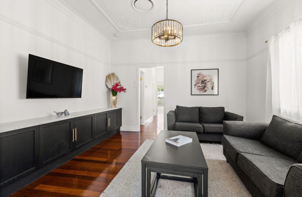 A modern renovated living room featuring a long, low-line matte black cabinet console with gold T-bar handles beneath a wall-mounted TV.